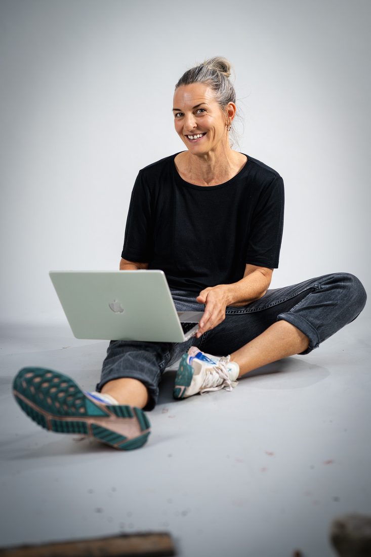 Silvia Kruetschnigg sitzt lächelnd mit Laptop am Boden